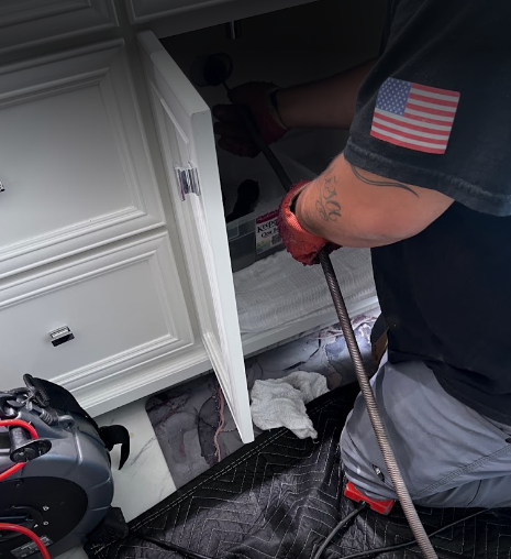  Plumber using a drain cleaning tool to inspect plumbing under a kitchen sink.