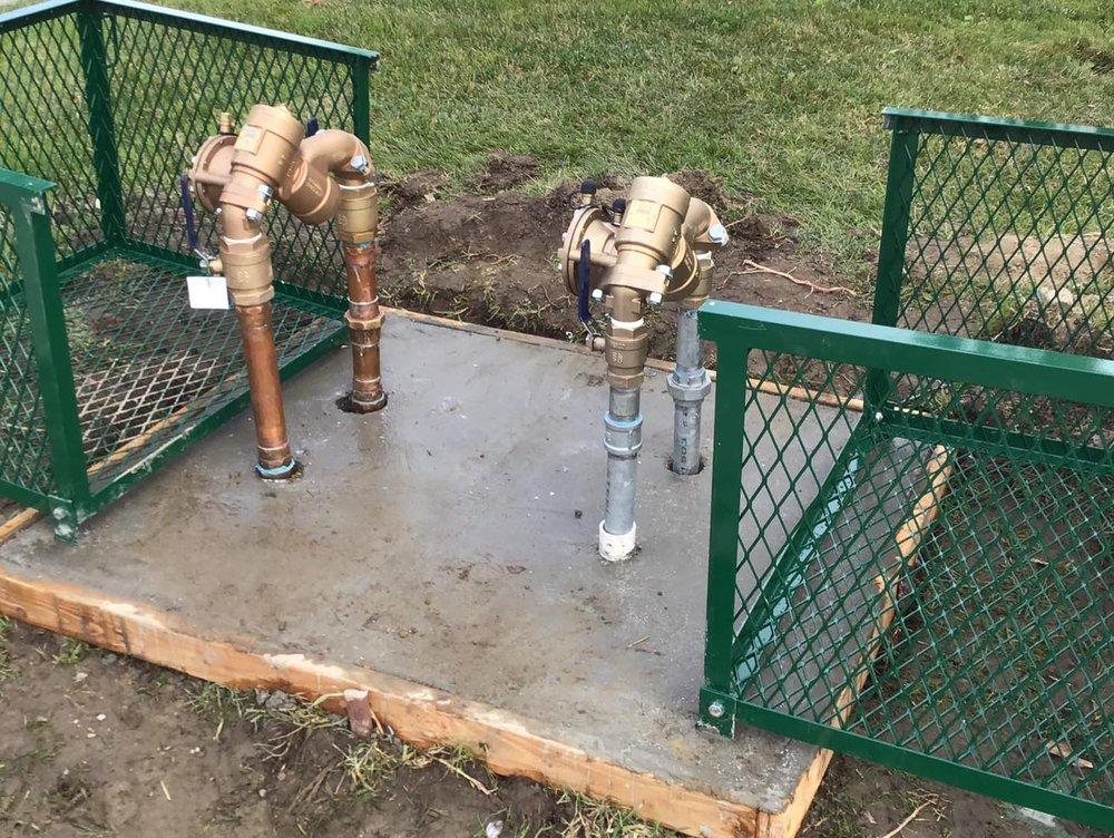 Two pipelines emerging from the ground surrounded by a green cage.