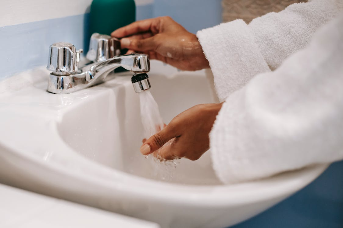 A woman in a robe water hands in the bathroom