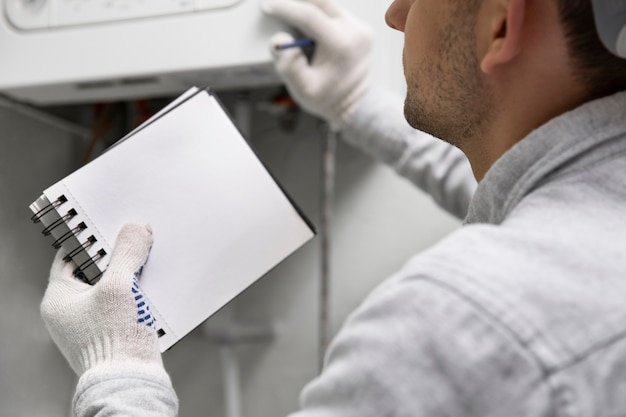 A plumber with a notepad in his hands inspecting a water heater