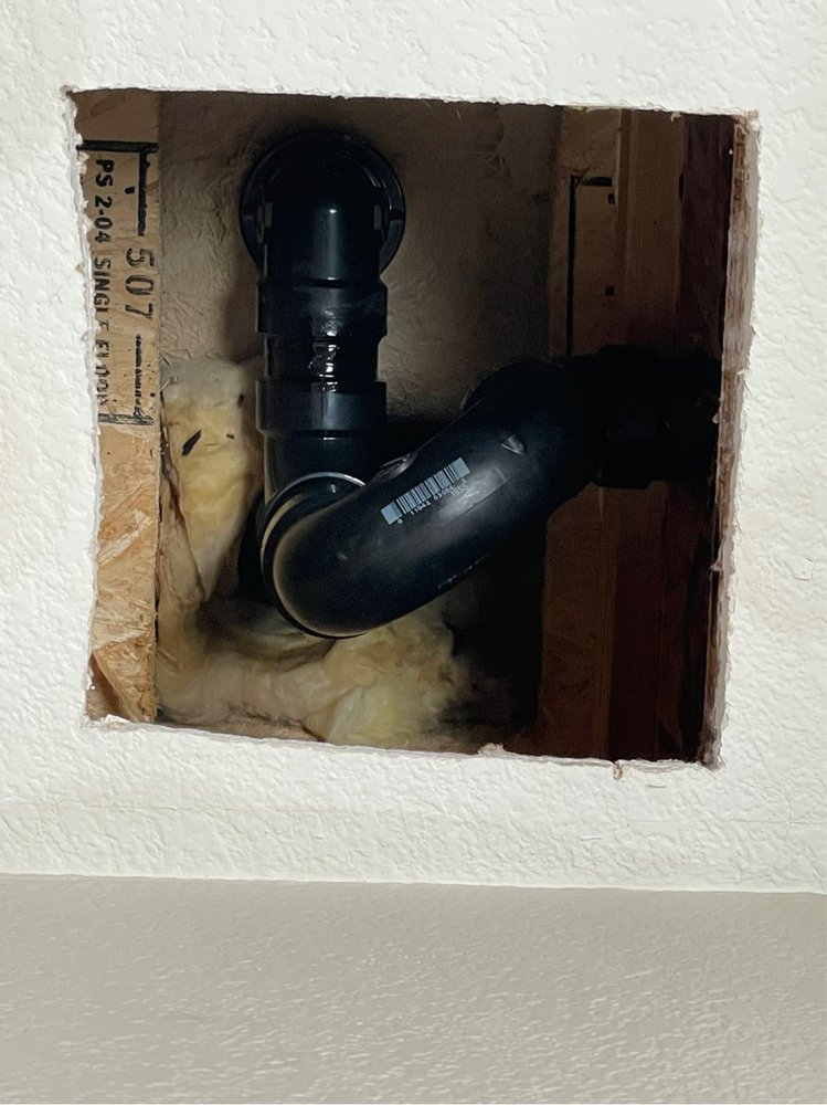 a black pipe with detected leaking issue being fixed behind a drywall