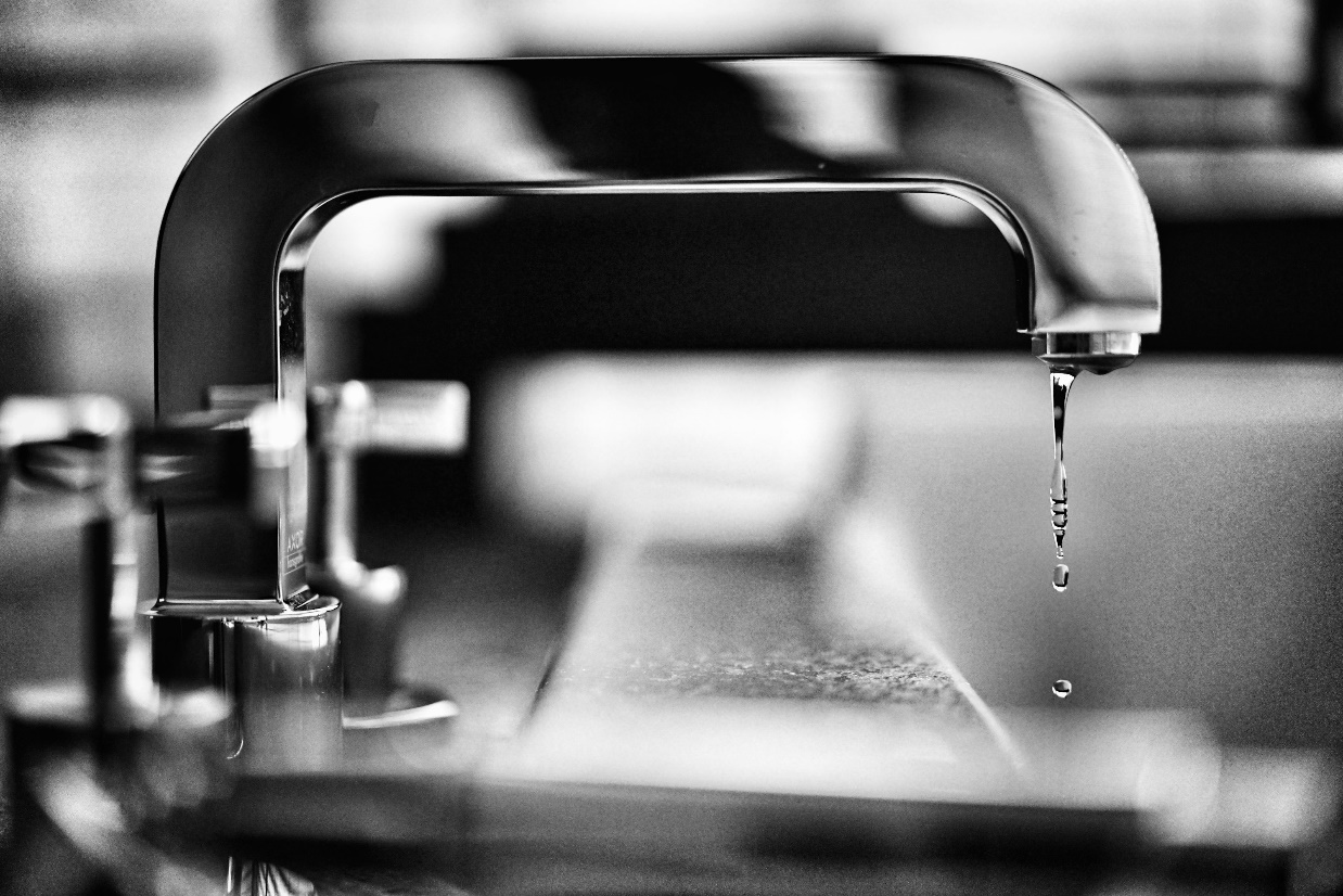 Close-up of a faucet dripping water into a stainless steel sink.