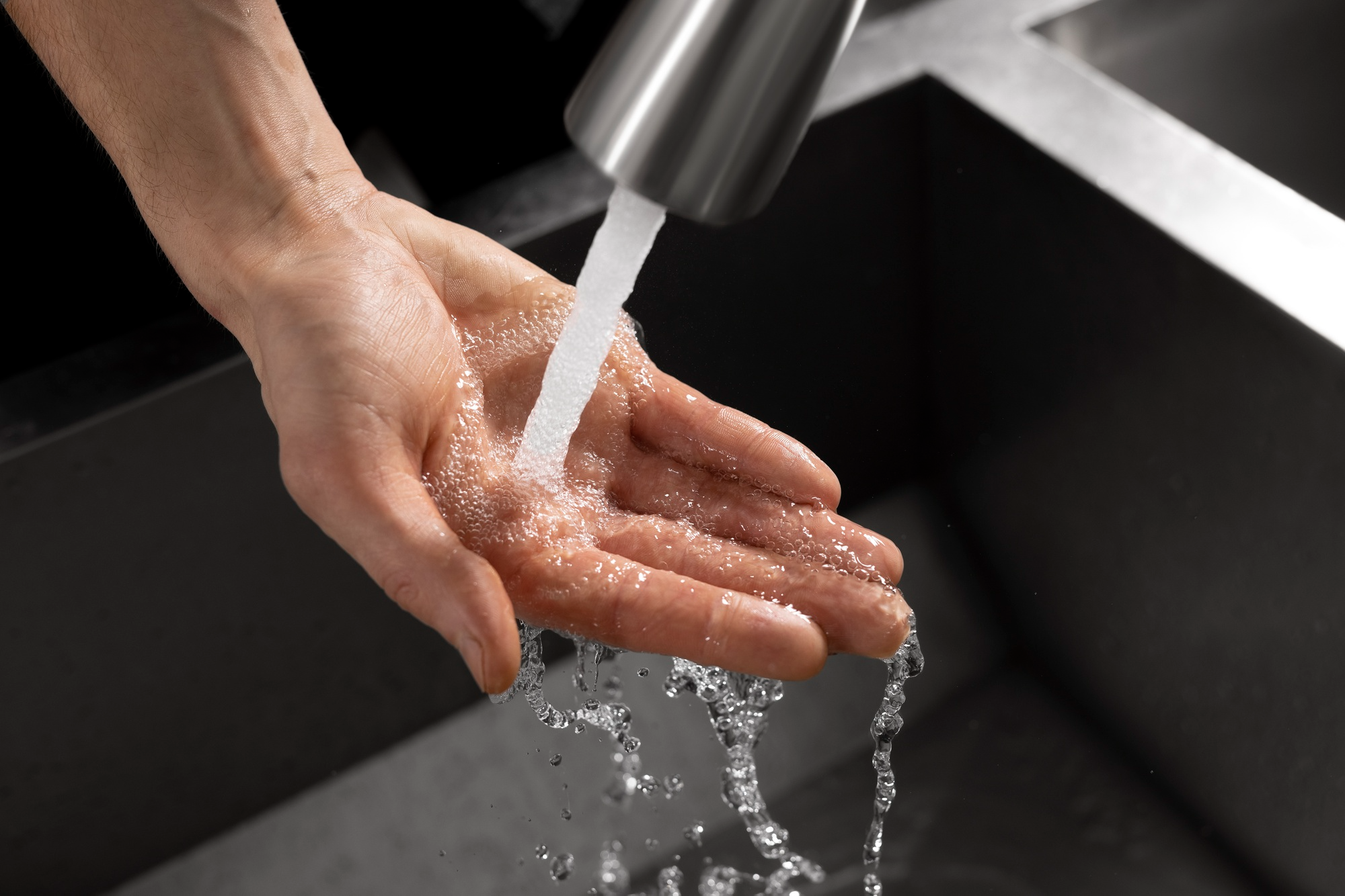 Individual washing hands under a weak water stream due to low water pressure.