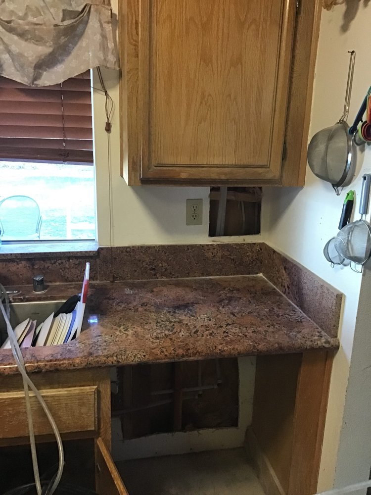 pipes being fixed behind the drywall of a kitchen and the cabinets around it