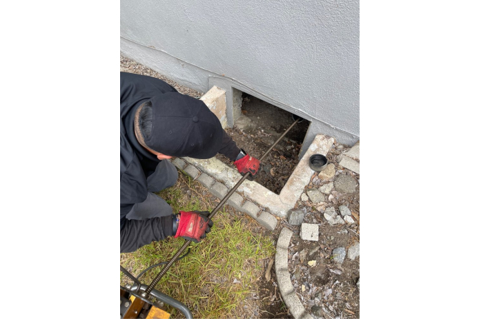 A man using a long tool to clean a household drain