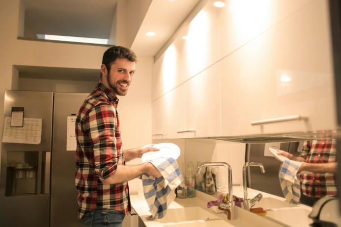 A man wiping dish plates clean in the kitchen sink.