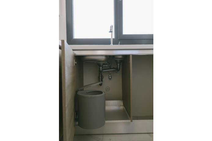Gray garbage can placed under a kitchen sink.