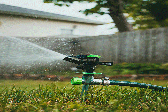 Garden sprinkler spraying water across green lawn
