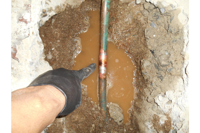 Exposed underground pipe with water leak causing soil damage
