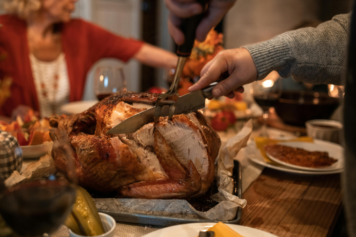 Person slicing a cooked turkey on a wooden cutting board.