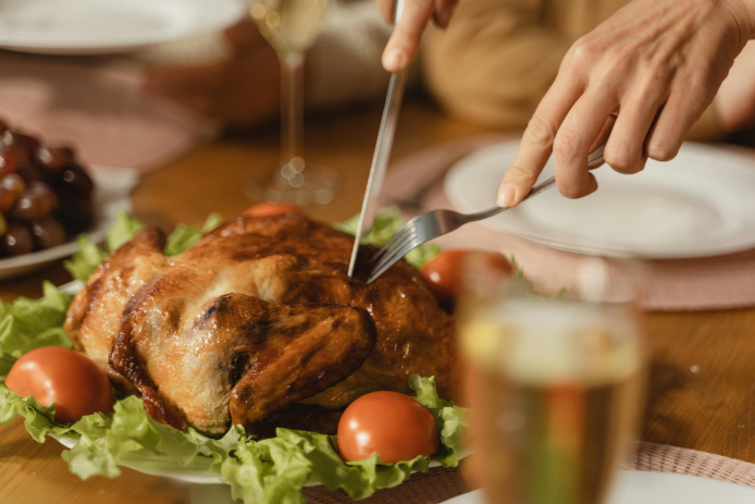 A person carving a cooked Thanksgiving turkey on a table.